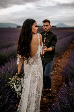 Les mariés dans un champs de lavande la mariée porte un bouquet moderne, mariage style boho, design floral Lilas Wood fleuriste mariage en Provence alpes côte d'azur - Photographie Chris and Ruth.
