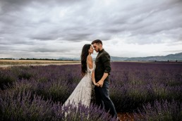 Les mariés dans un champs de lavande la mariée porte un bouquet moderne, mariage style boho, design floral Lilas Wood fleuriste mariage en Provence alpes côte d'azur - Photographie Chris and Ruth.